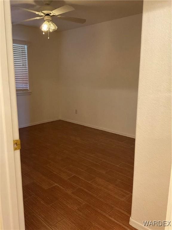 spare room with baseboards, a ceiling fan, and dark wood-type flooring