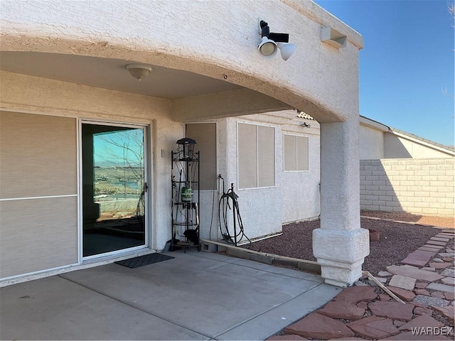 doorway to property with stucco siding, fence, and a patio