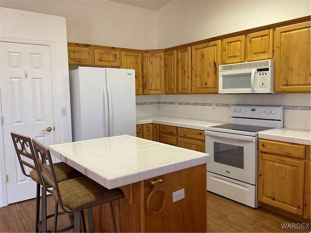 kitchen featuring a center island, dark wood-style flooring, tile counters, tasteful backsplash, and white appliances