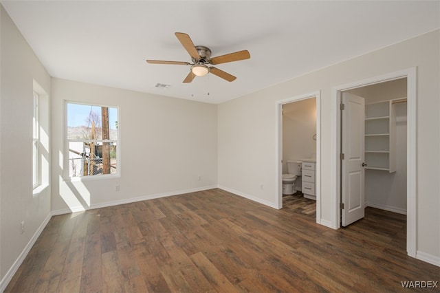 unfurnished bedroom with a walk in closet, dark wood-style flooring, visible vents, and baseboards