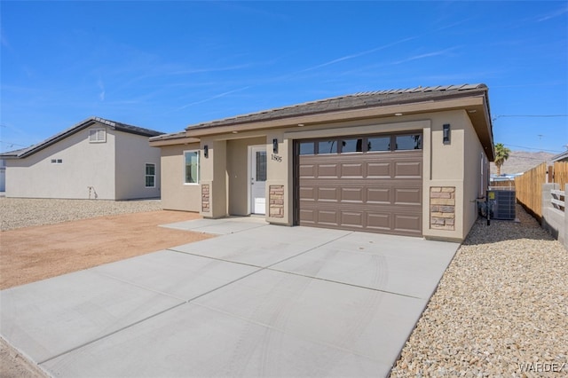 view of front of home with stucco siding, concrete driveway, an attached garage, central AC, and fence