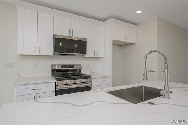 kitchen with stainless steel appliances, white cabinetry, a sink, and light stone countertops