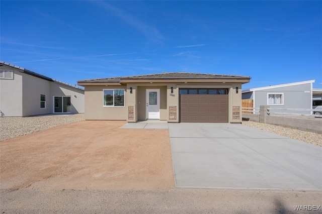 prairie-style house featuring concrete driveway, fence, an attached garage, and stucco siding