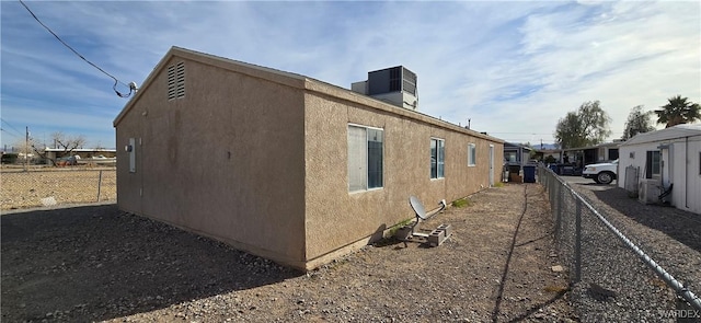 view of side of property with central AC, fence, and stucco siding