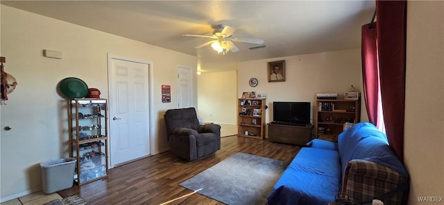 living room featuring a ceiling fan, visible vents, baseboards, and wood finished floors