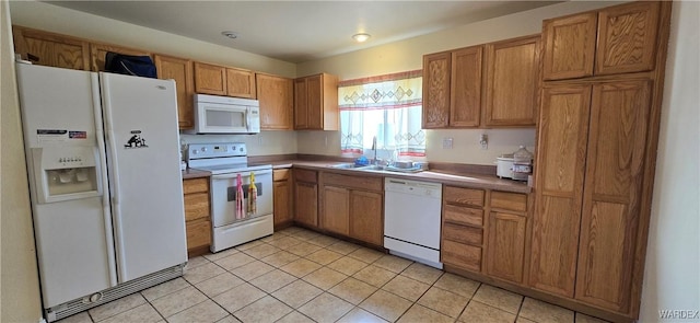 kitchen featuring brown cabinets, white appliances, light tile patterned flooring, and a sink