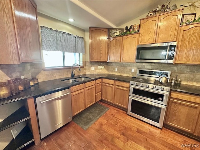 kitchen featuring appliances with stainless steel finishes, dark countertops, a sink, and dark wood finished floors