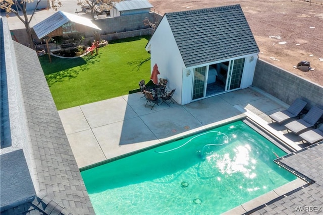 view of swimming pool featuring a patio, fence, a lawn, and an outbuilding