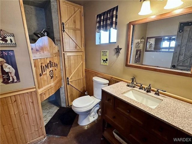 half bathroom featuring a wainscoted wall, wood walls, vanity, and toilet