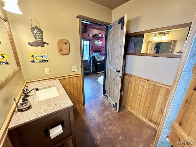 bathroom with wood walls, concrete floors, wainscoting, and vanity