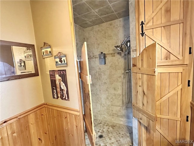 bathroom with a stall shower, a wainscoted wall, and wood walls