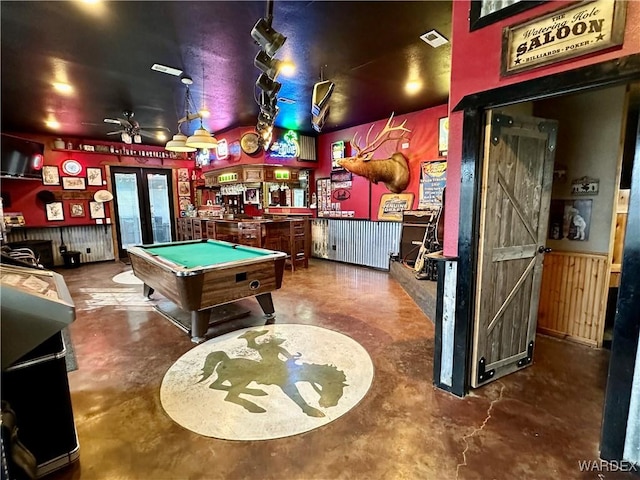 playroom with french doors, a wainscoted wall, pool table, a bar, and unfinished concrete floors