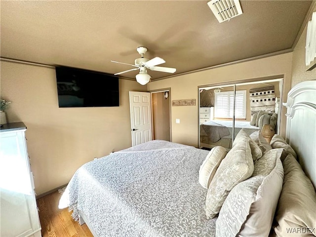 bedroom with ceiling fan, light wood-style flooring, visible vents, baseboards, and a closet