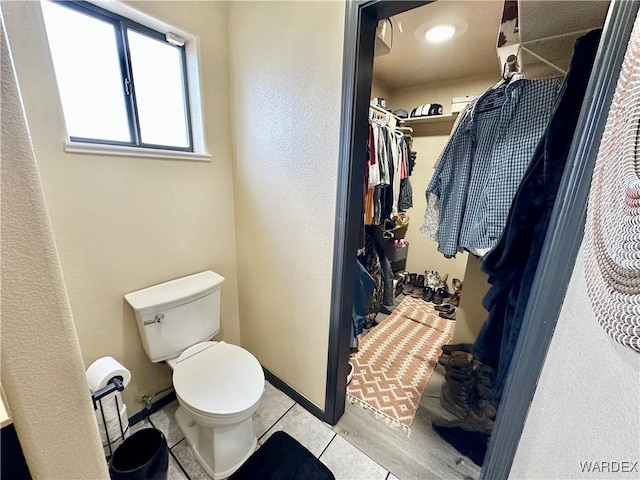 bathroom featuring a spacious closet, tile patterned flooring, toilet, and baseboards