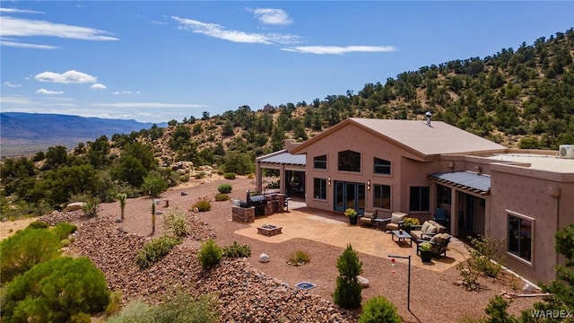 rear view of house featuring stucco siding, a fire pit, a view of trees, and a patio