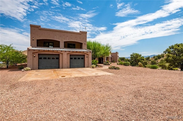 view of front facade featuring a garage, concrete driveway, metal roof, a standing seam roof, and stucco siding