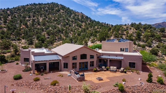 back of property with an outdoor living space with a fire pit, a forest view, a patio area, a mountain view, and stucco siding