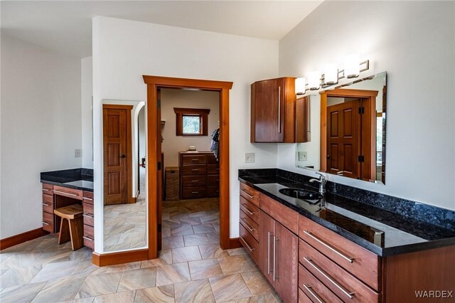 kitchen with dark stone countertops, a sink, and baseboards