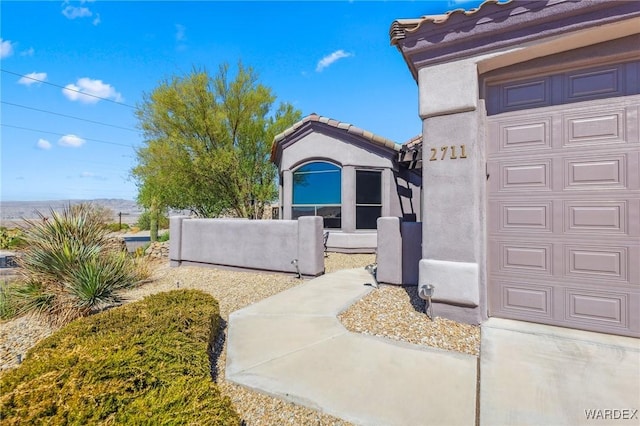 view of property exterior featuring a garage, a tile roof, fence, and stucco siding