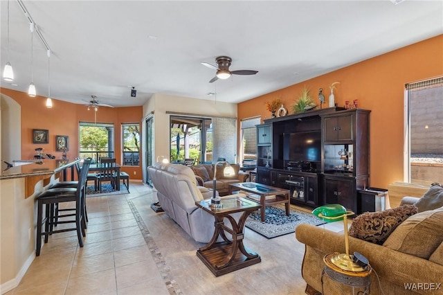 living area featuring light tile patterned floors, rail lighting, a ceiling fan, and baseboards