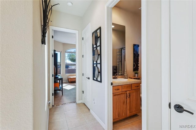 hall featuring a sink, baseboards, and light tile patterned floors