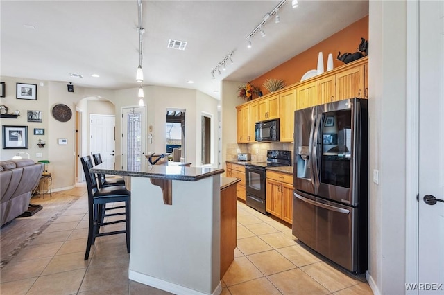 kitchen with a center island with sink, a breakfast bar area, dark countertops, light tile patterned flooring, and black appliances