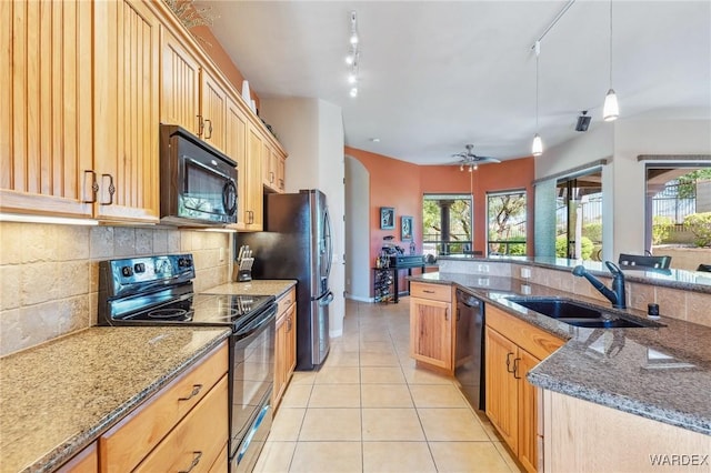 kitchen with light tile patterned floors, dark stone counters, hanging light fixtures, black appliances, and a sink