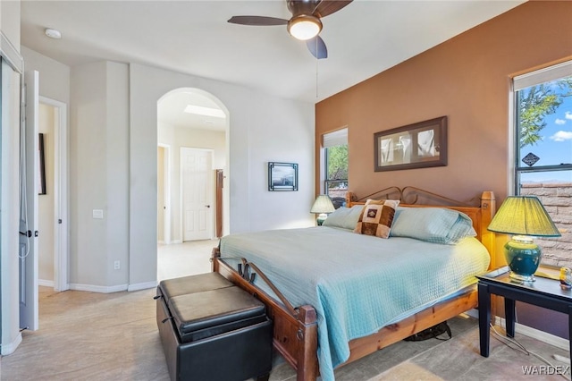 bedroom featuring arched walkways, multiple windows, a ceiling fan, and baseboards