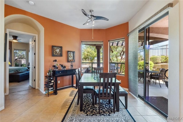 dining area featuring a healthy amount of sunlight, light tile patterned floors, arched walkways, and a ceiling fan