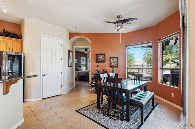 dining room with a ceiling fan, arched walkways, baseboards, and light tile patterned floors