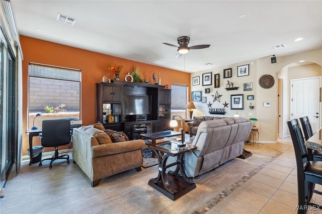 living room featuring arched walkways, baseboards, visible vents, and a ceiling fan