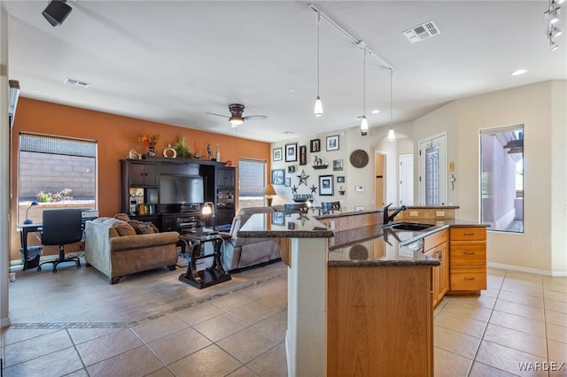 kitchen with open floor plan, a kitchen island with sink, visible vents, and decorative light fixtures