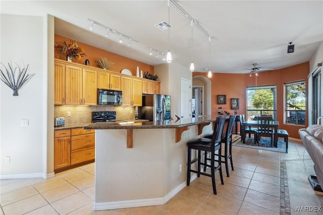 kitchen with visible vents, an island with sink, black microwave, stainless steel fridge, and a kitchen breakfast bar