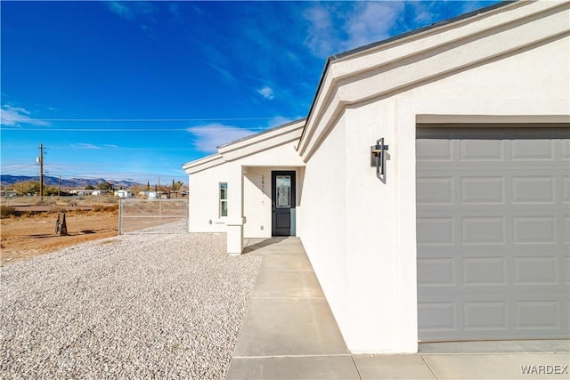 doorway to property with an attached garage, fence, and stucco siding