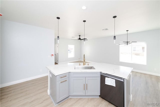 kitchen featuring dishwasher, light stone counters, open floor plan, a kitchen island with sink, and a sink