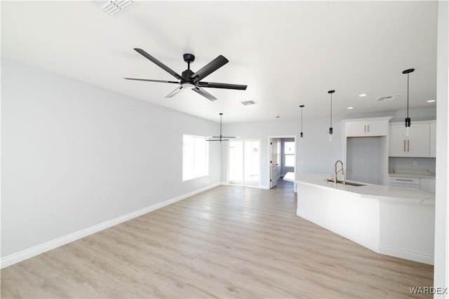 interior space featuring ceiling fan, a sink, visible vents, baseboards, and light wood-type flooring