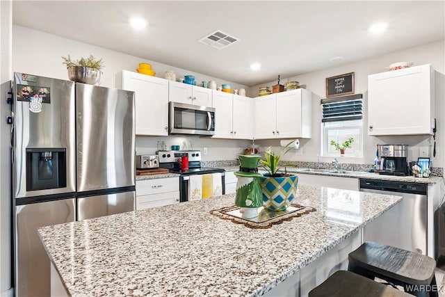 kitchen featuring visible vents, a kitchen island, stainless steel appliances, white cabinets, and a kitchen bar