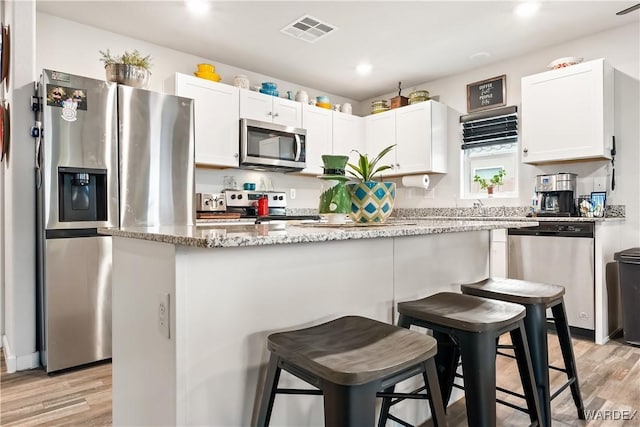 kitchen featuring visible vents, a kitchen island, light wood-style flooring, appliances with stainless steel finishes, and white cabinets