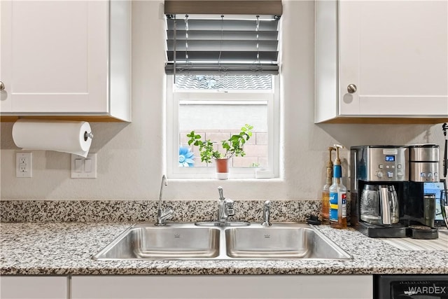 kitchen featuring light stone counters, dishwasher, white cabinetry, and a sink