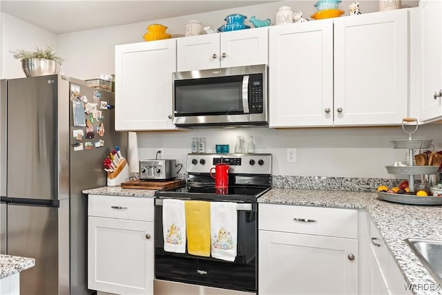 kitchen featuring light stone counters, white cabinets, appliances with stainless steel finishes, and a sink