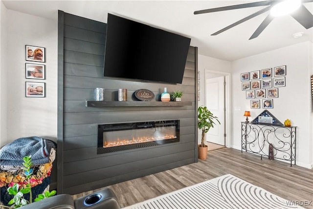 living area featuring a ceiling fan, light wood-style floors, and a large fireplace