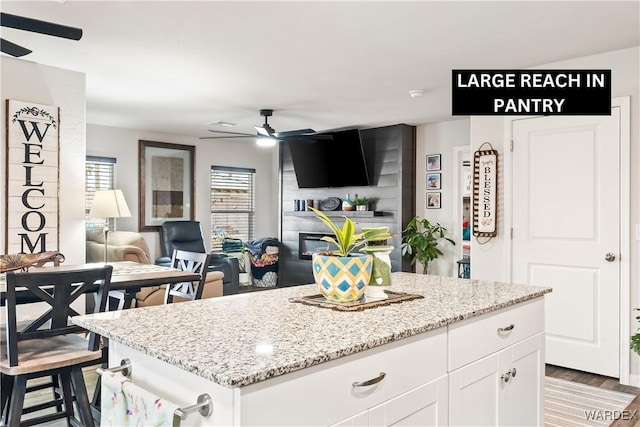 kitchen featuring white cabinets, a center island, a ceiling fan, and light stone countertops