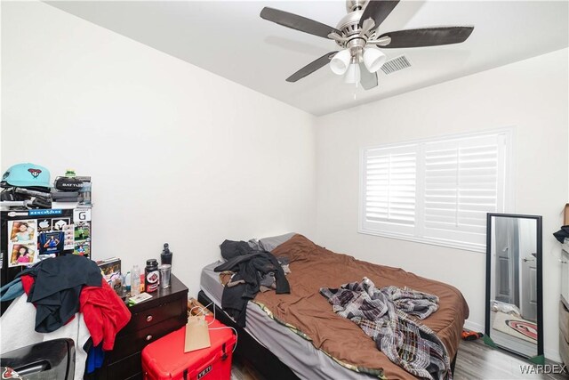 bedroom with ceiling fan, visible vents, and wood finished floors