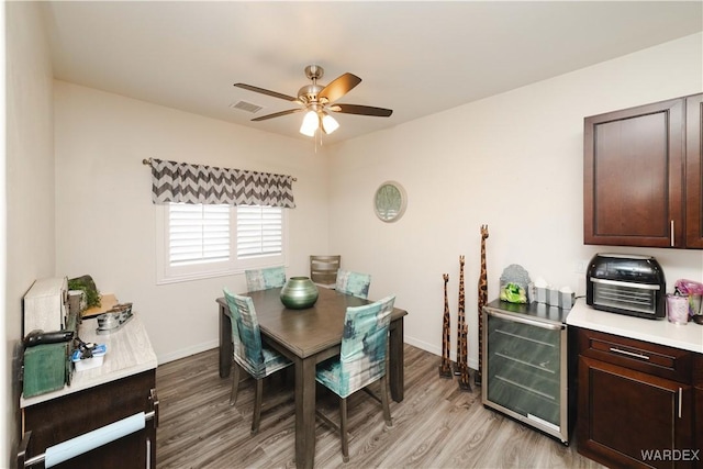 dining space featuring baseboards, visible vents, ceiling fan, wine cooler, and light wood-type flooring