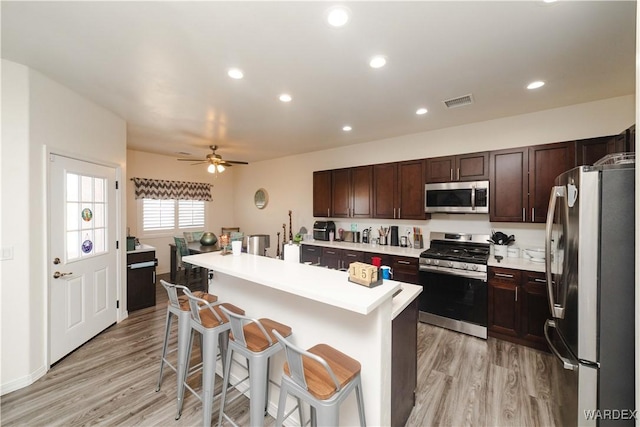 kitchen featuring light wood finished floors, a center island with sink, a breakfast bar, stainless steel appliances, and light countertops