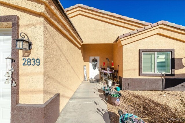 entrance to property featuring a patio area, a tiled roof, and stucco siding