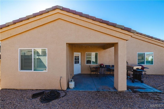 rear view of house with a patio area, a tile roof, and stucco siding