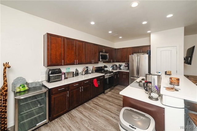 kitchen featuring beverage cooler, appliances with stainless steel finishes, light countertops, light wood-type flooring, and recessed lighting