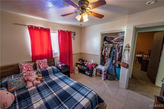 bedroom featuring a textured ceiling, light tile patterned floors, a closet, and a ceiling fan