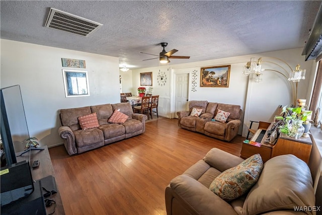 living area featuring a textured ceiling, ceiling fan, wood finished floors, and visible vents